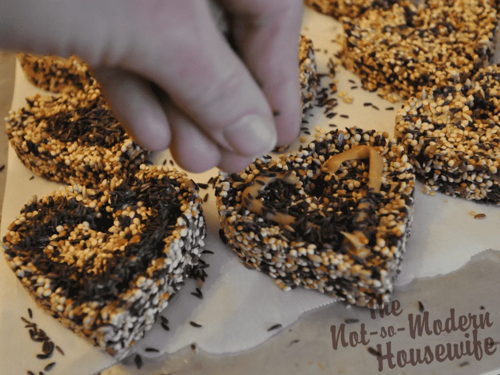 Easy DIY Birdseed Ornaments | The Not so Modern Housewife sprinkling black Nyjer birdseed onto peanut butter for birdseed ornaments
