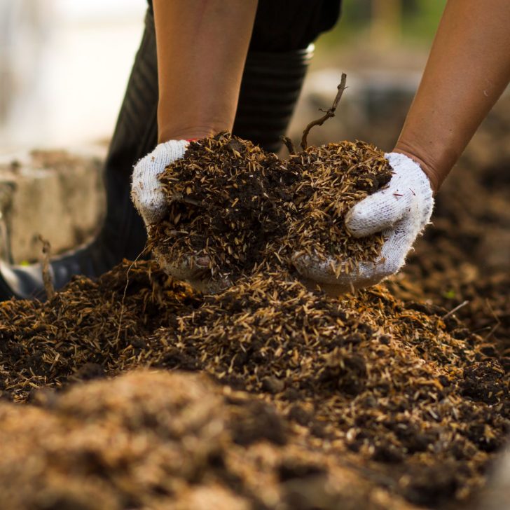 gloved hands spreading finished compost -  harvesting and utilizing your homemade compost - how to compost