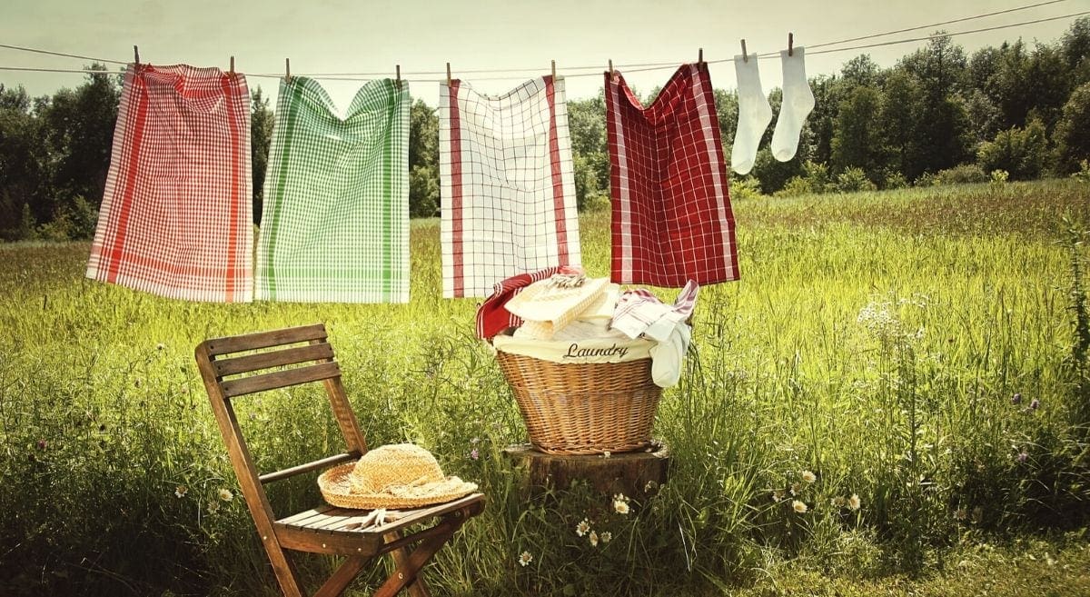 laundry hung on clothesline with laundry basket, wooden chair, and straw hat, country field in background