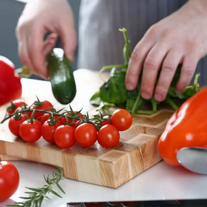 hands arranging cucumbers, basil, and tomatoes on a cutting board - homesteading ideas