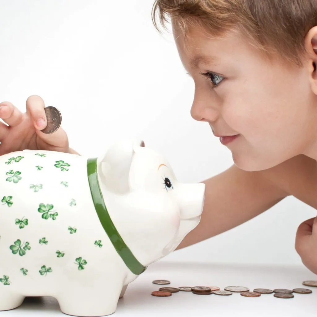 Kid putting coins in a piggy bank - financial literacy for kids