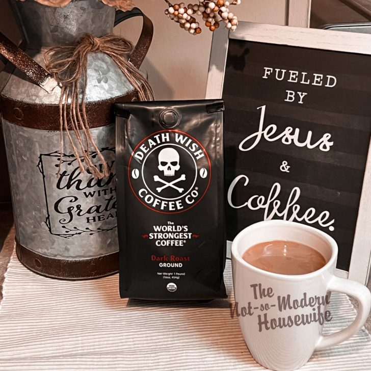 Death Wish Coffee Dark Roast Ground Coffee with white mug and Fueled by Jesus & Coffee sign