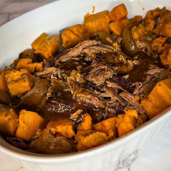 roast beef with sweet potatoes and apples in a white ceramic serving bowl