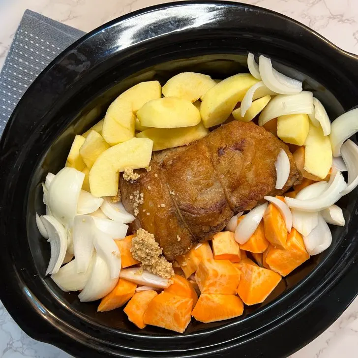 browned beef pot roast in slow cooker with sweet potatoes, apples, onions, and garlic