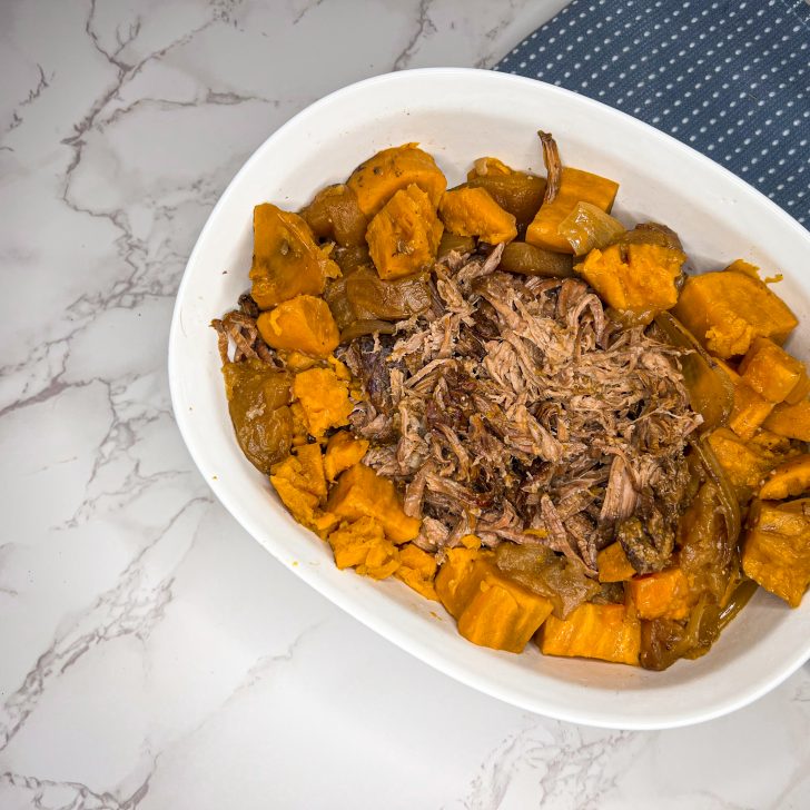 roast beef and sweet potatoes in a white ceramic serving dish on a white marble counter with a blue dish towel