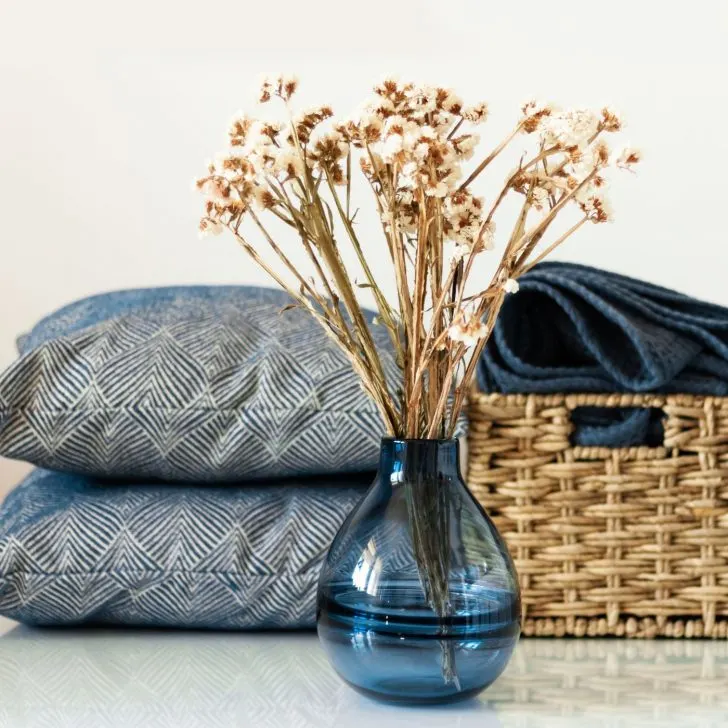 home decor - blue throw pillows, blue vase with dried flowers, and wicker basket with blue blanket - Christmas gift ideas for housewives