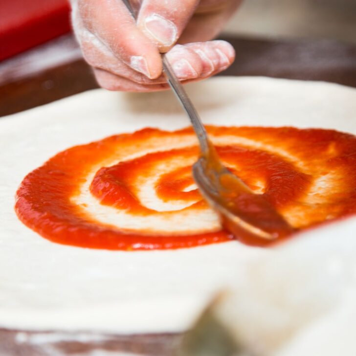 spreading sauce on pizza crust with a spoon - easy pizza dough