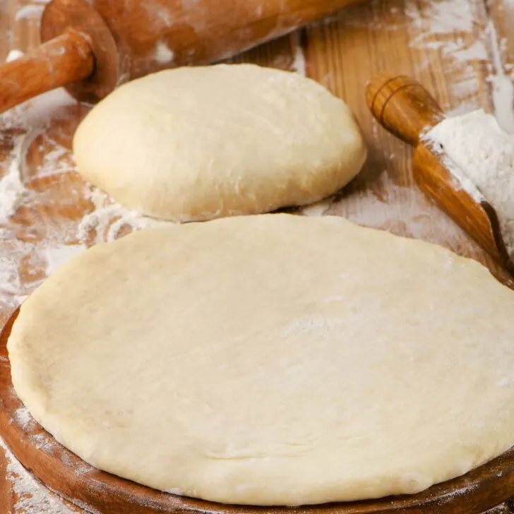homemade pizza crust shaped on cutting board with rolling pin - easy pizza dough
