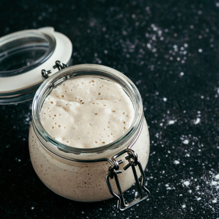 active sourdough starter in a glass jar with a flipped open top on a black surface with flour dust